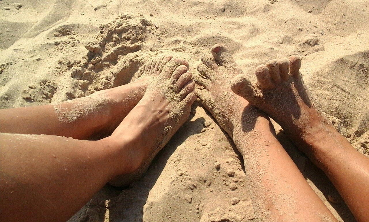 the legs of two people sitting in a sand on  a beach