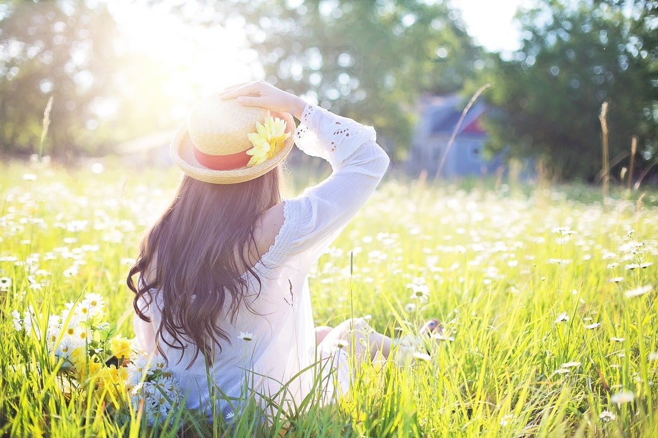 a kid sitting in the nature with a hat on her head