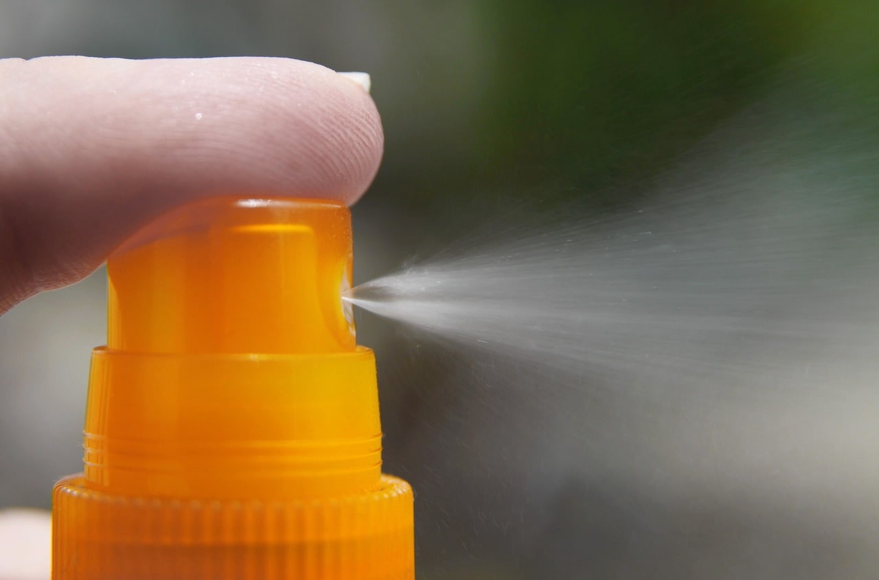 a person pushes the button of a sunscreen spray