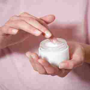 a woman is taking moisturizer from a container