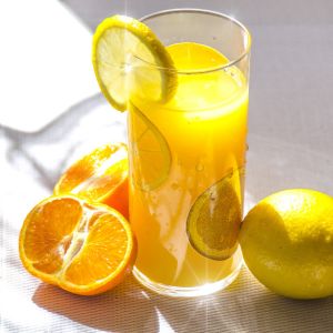 a glass of lemon juice with a couple of lemons around it 